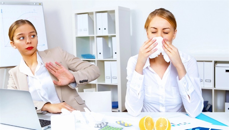 Una mujer estornuda en un pañuelo y otra persona se da la vuelta